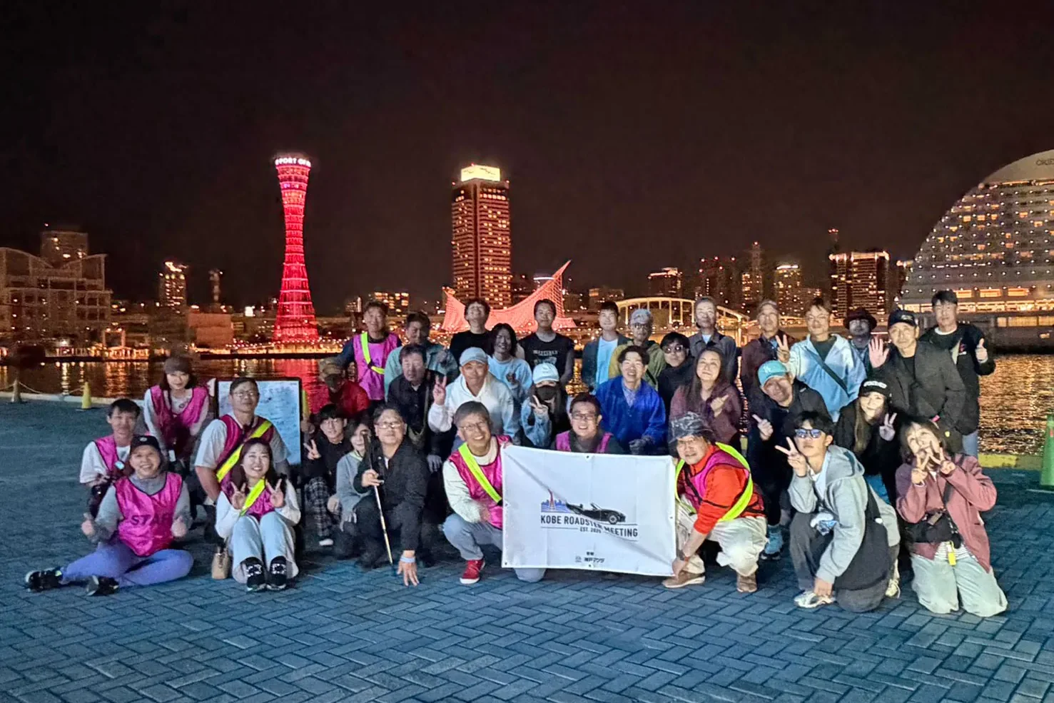 Group photo of KRM staff gathered against the Kobe night skyline